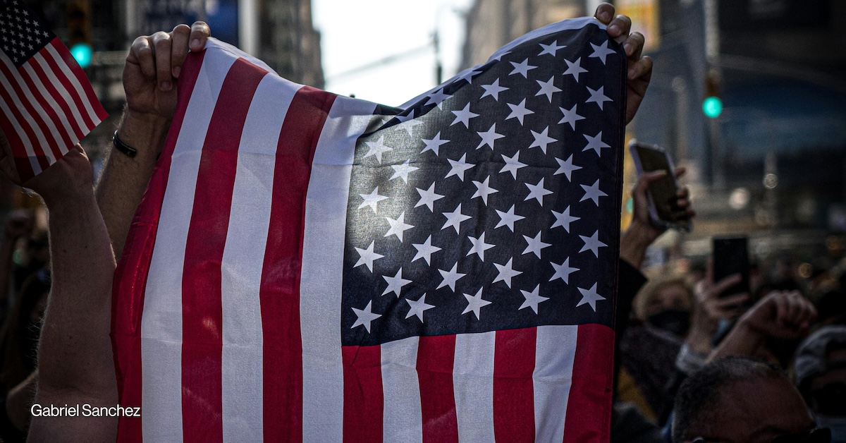 A person waves the U.S.
 flag in the middle of a crowd.